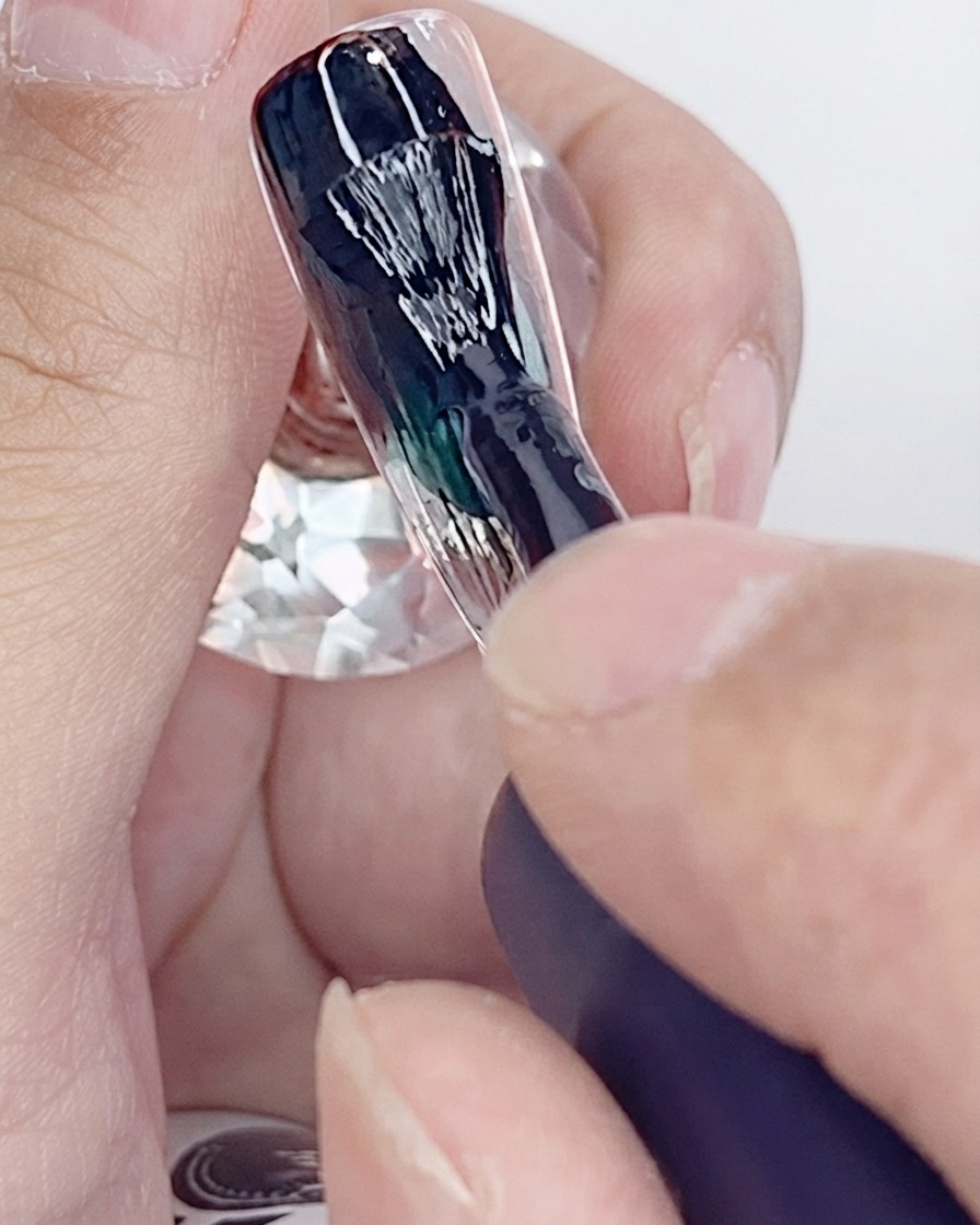 Un pinceau appliquant la première couche de vernis gel noir sur une capsule dongle artificielle.