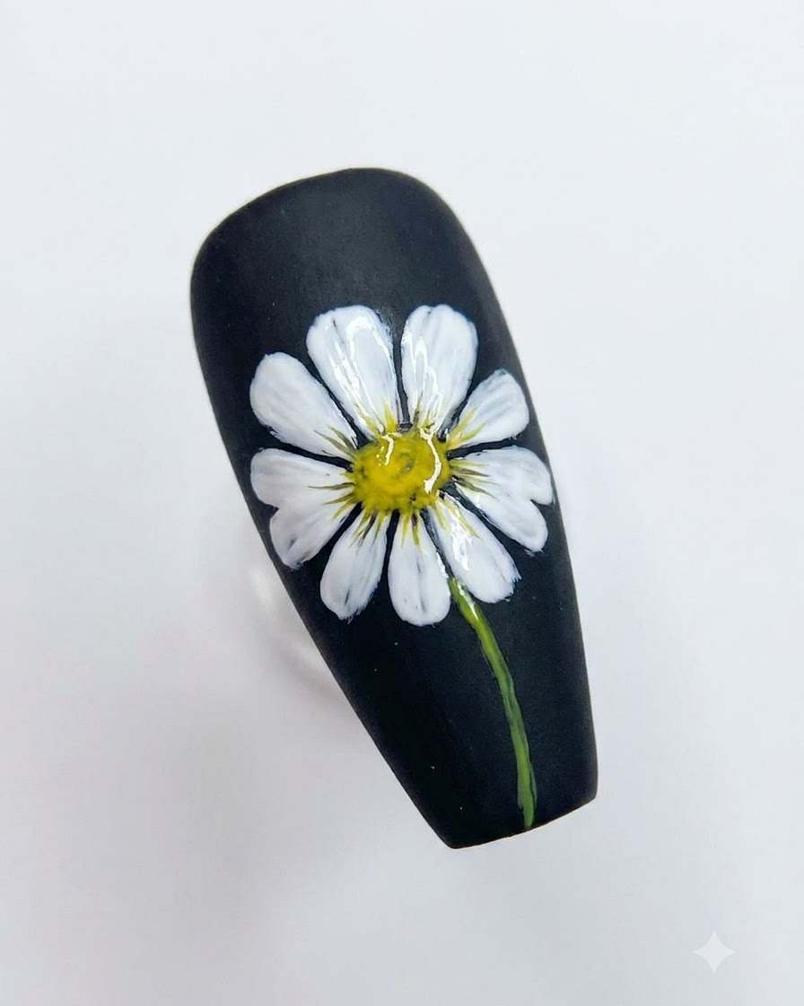 Un nail art noir terminé présentant une marguerite blanche détaillée avec un cœur jaune vif et une tige verte.