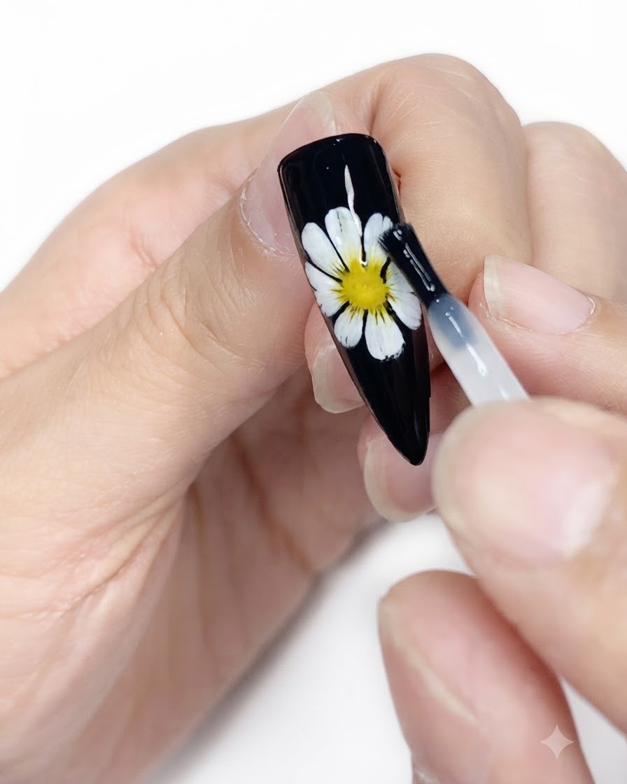 Une lingette nettoyante purifiant la surface dun ongle noir fini orné dun nail art marguerite blanche et jaune.