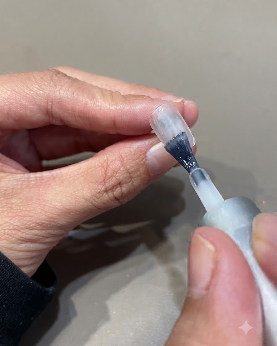 Un pinceau à ongles appliquant une deuxième couche de vernis gel blanc translucide sur une plaque dongle naturel.