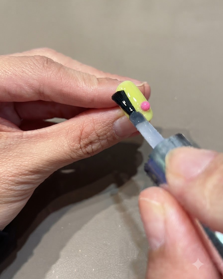 Un pinceau appliquant un top coat transparent sur la surface dun ongle doté dune décoration de sphère rose.