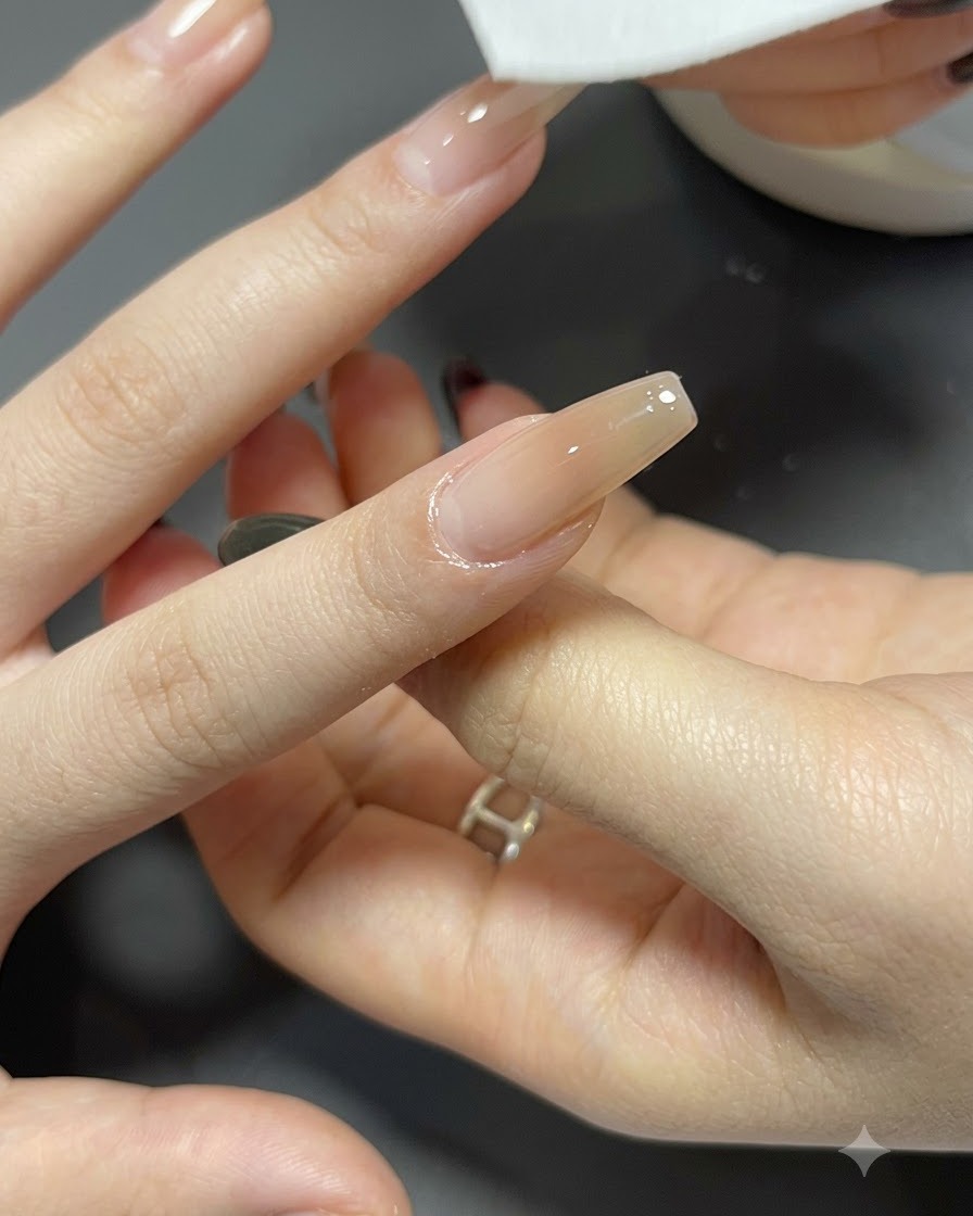 Une lingette non pelucheuse nettoyant la surface dun ongle long en forme de cercueil avec un dégradé terminé.