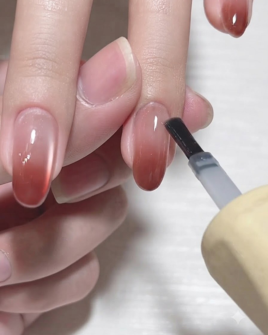 Un pinceau de flacon de gel appliquant un top coat transparent brillant sur un ongle en dégradé terminé.