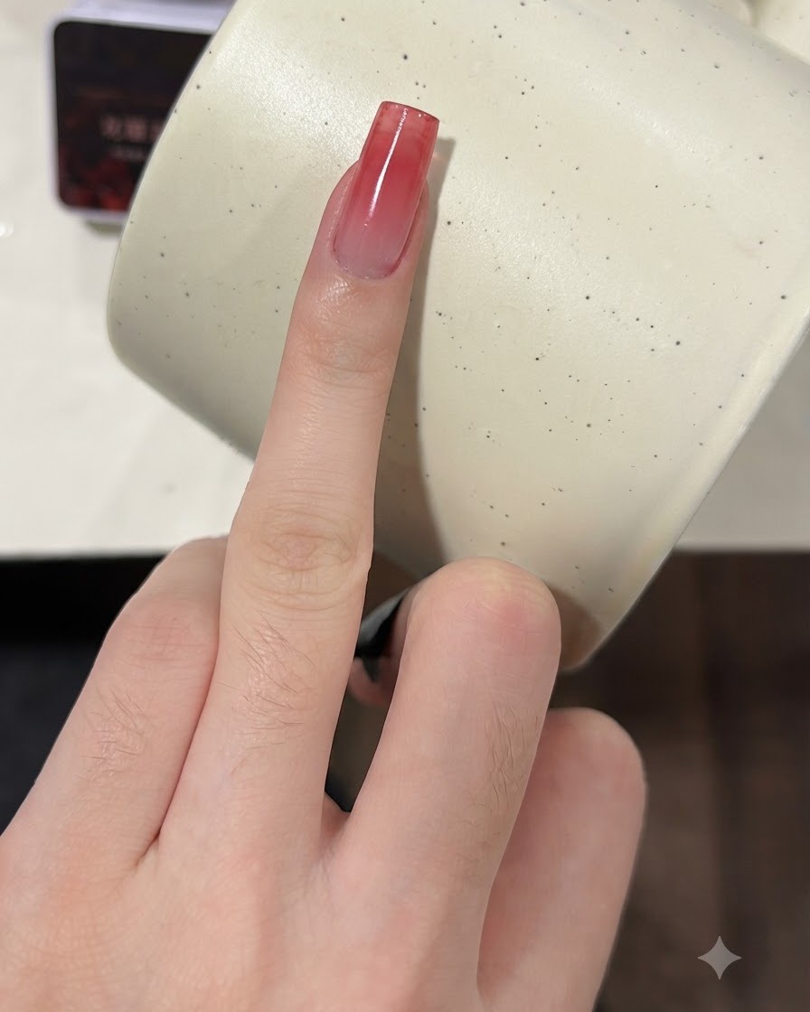 Un doigt avec un ongle dégradé rouge bordeaux sur lequel on presse une éponge pour une seconde couche.