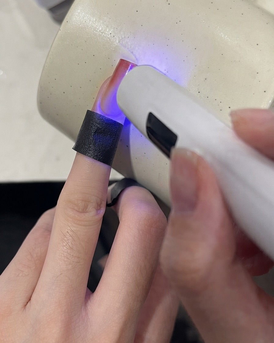Une mini lampe UV catalysant le bout dun ongle dégradé avec une finition rouge bordeaux.