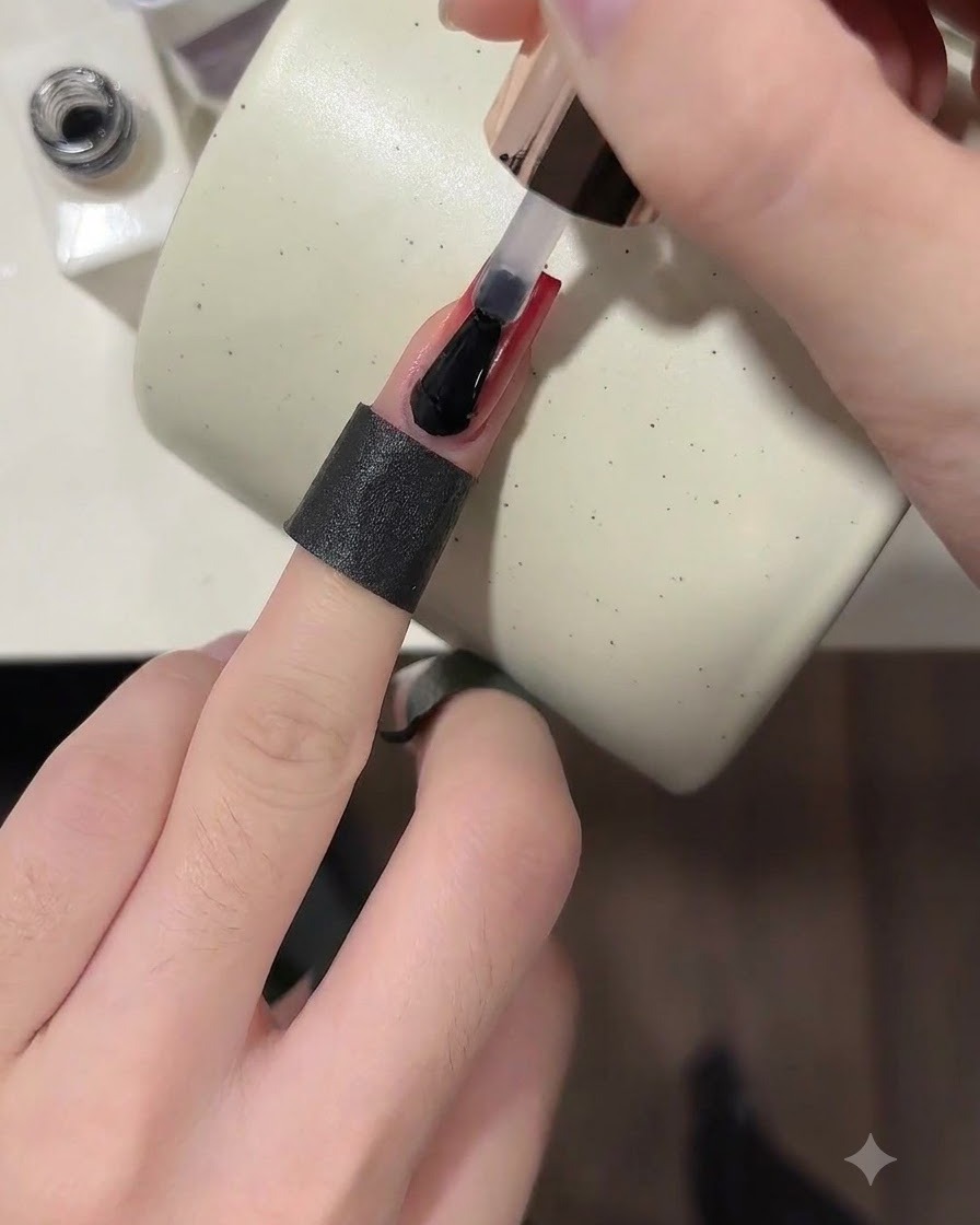 Un pinceau appliquant un top coat transparent brillant sur un ongle ombré rouge bordeaux terminé.