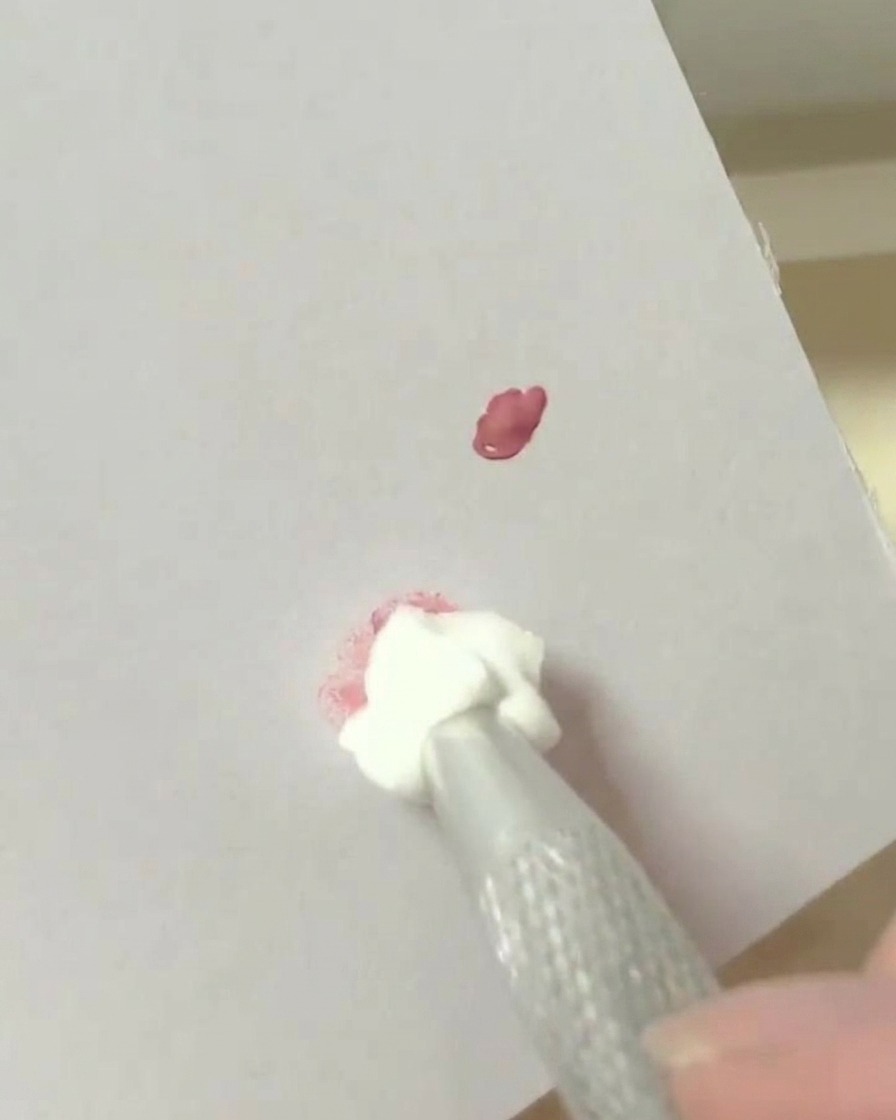 Un outil éponge de maquillage tapotant dans une tache de pigment mélangée sur une surface de palette blanche.