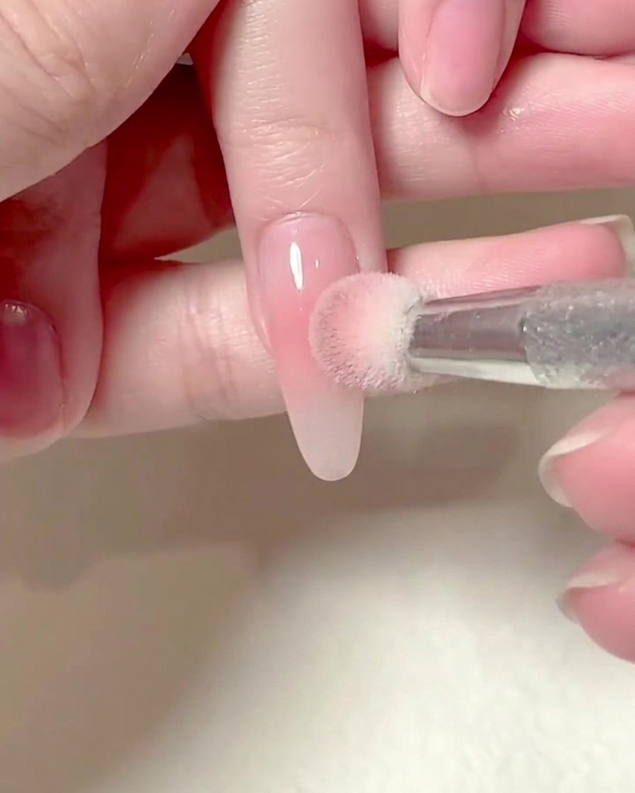 Une éponge carrée tenue par une main tapotant délicatement du gel blush rose sur un onglet allongé.