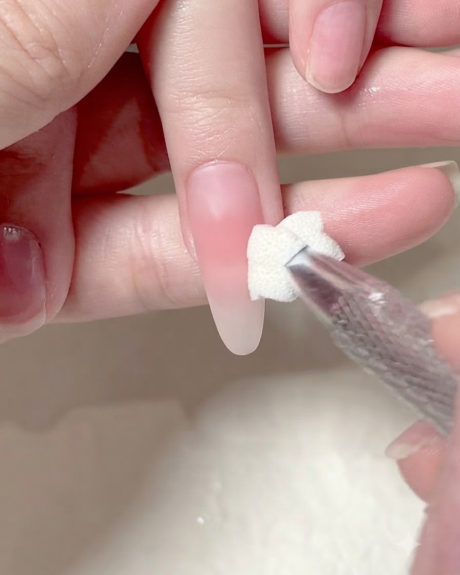 Un applicateur éponge tapotant une deuxième couche de gel rose sur le centre dun ongle manucuré.
