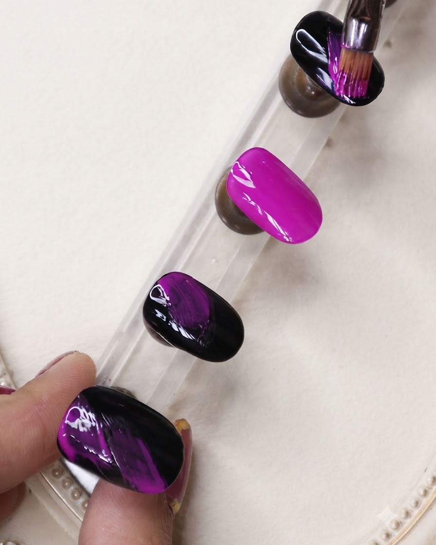 Un pinceau fin appliquant des stries de gel noir sur un ongle violet néon vibrant sur un support de présentation.