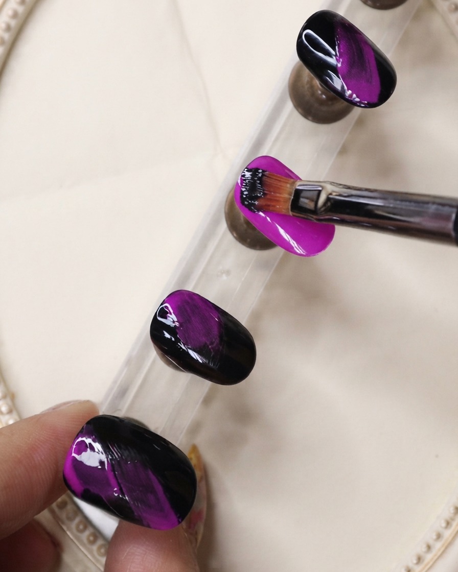 Un pinceau fin appliquant du gel noir en traits texturés sur un ongle violet néon.