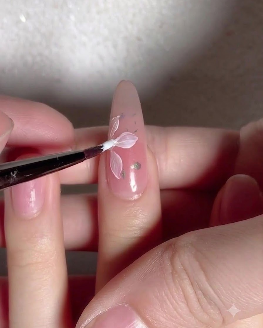 Un pinceau appliquant une couche de top coat transparent et brillant sur un ongle décoré de fleurs et de flocons.
