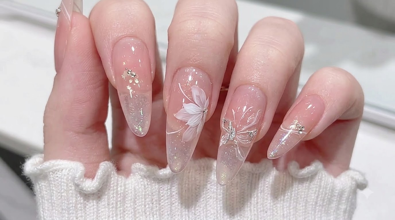 Ongles nude translucides en amande ornés dun dégradé blush rose, de paillettes aurora et dun délicat nail art floral blanc.