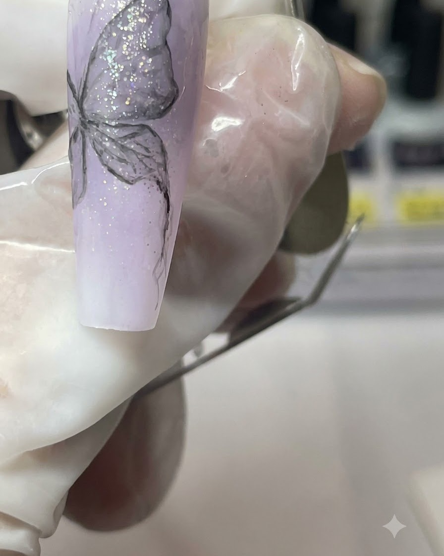 Gros plan dun doigt manucuré tenant la capsule dongle violette tout en détaillant le corps du papillon.