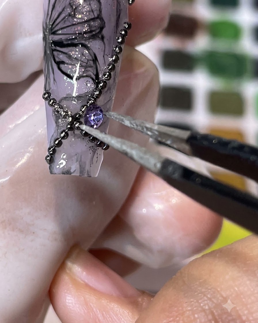 Une paire de pinces plaquant un strass violet à dos pointu sur une surface dongle décorée.