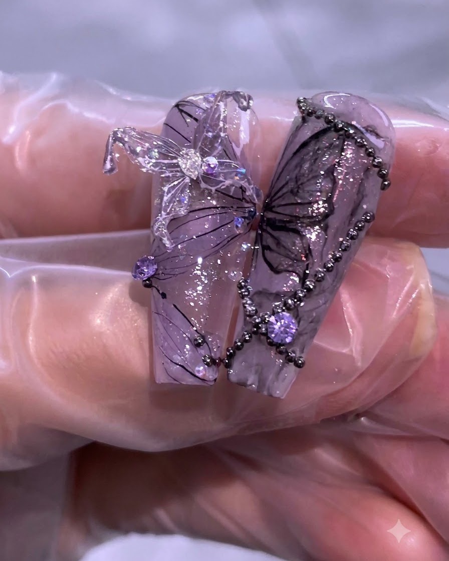 Gros plan de nail art violet et noir complété présentant des détails de papillons, des strass et de fines lignes de fil.
