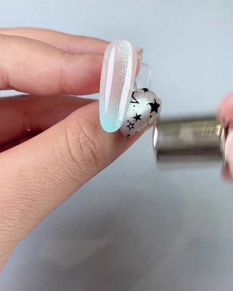 Un bâtonnet aimanté tenu près du côté dun ongle pour attirer et façonner une large bande lumineuse cat-eye.