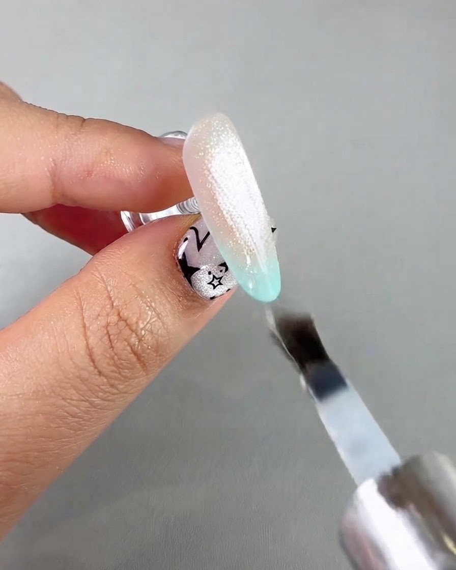 Un pinceau à ongles appliquant un top coat de scellement transparent sur une extension dongle cat-eye scintillante.