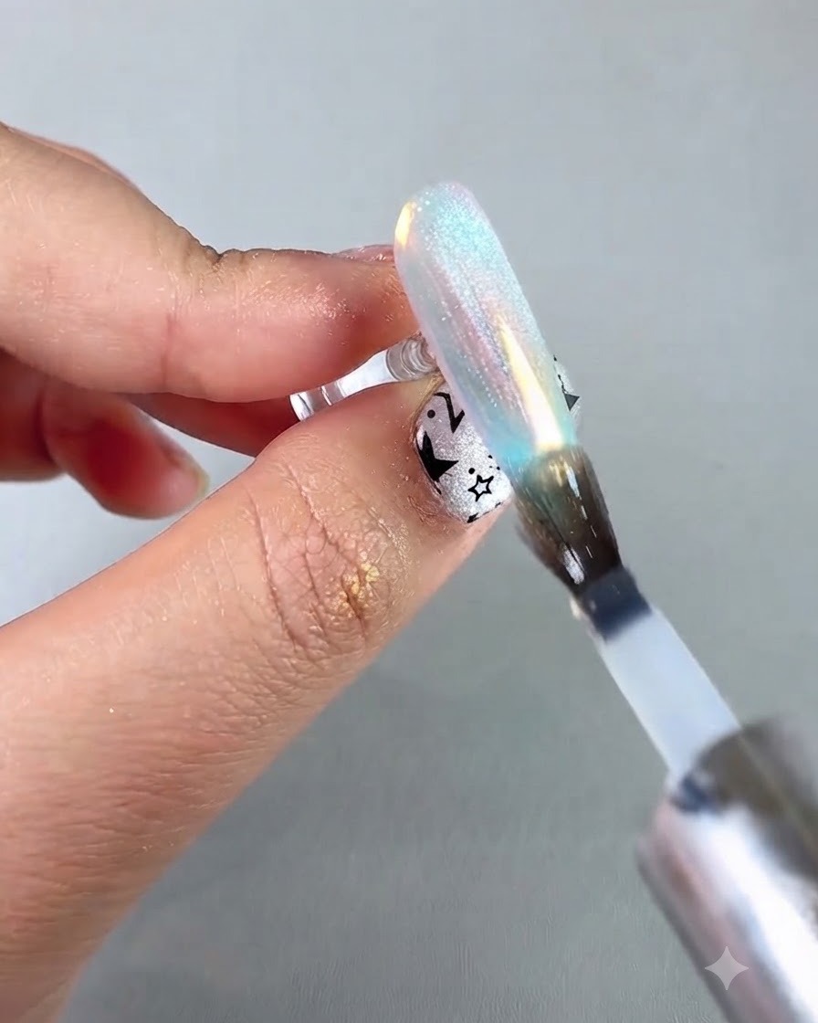 Un pinceau à ongles appliquant un top coat de scellement protecteur sur un ongle chrome aurora irisé.