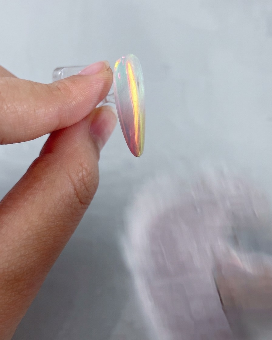 Un pinceau doux et duveteux balayant la poudre métallique résiduelle dun ongle à finition chrome brillante.