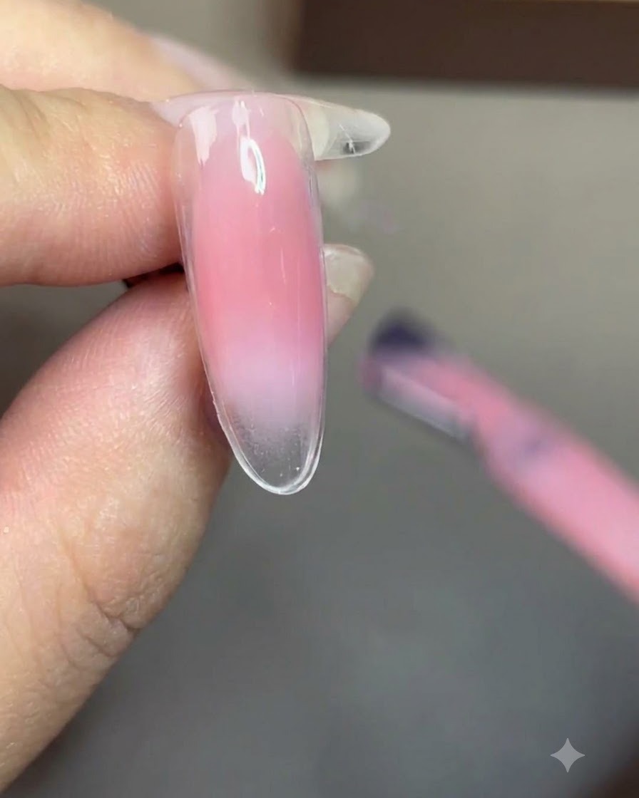 Un pinceau appliquant un gel nude diaphane de manière homogène sur tout longle.