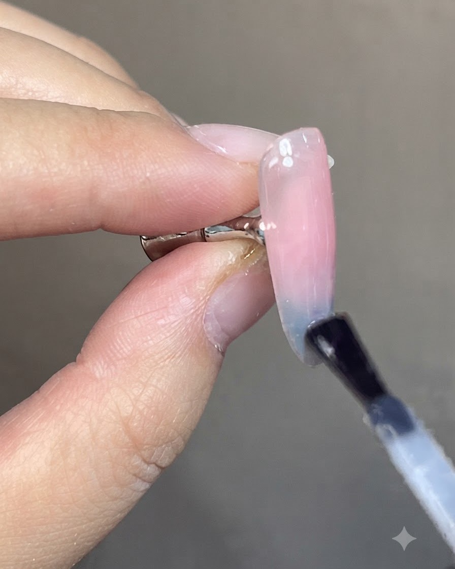 Un pinceau appliquant un top coat brillant transparent sur un design dongles en dégradé cat-eye bleu et rose terminé.