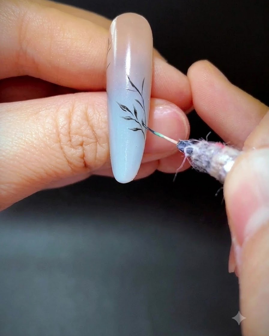 Un pinceau fin peignant de délicates branches secondaires sur un ongle en dégradé.