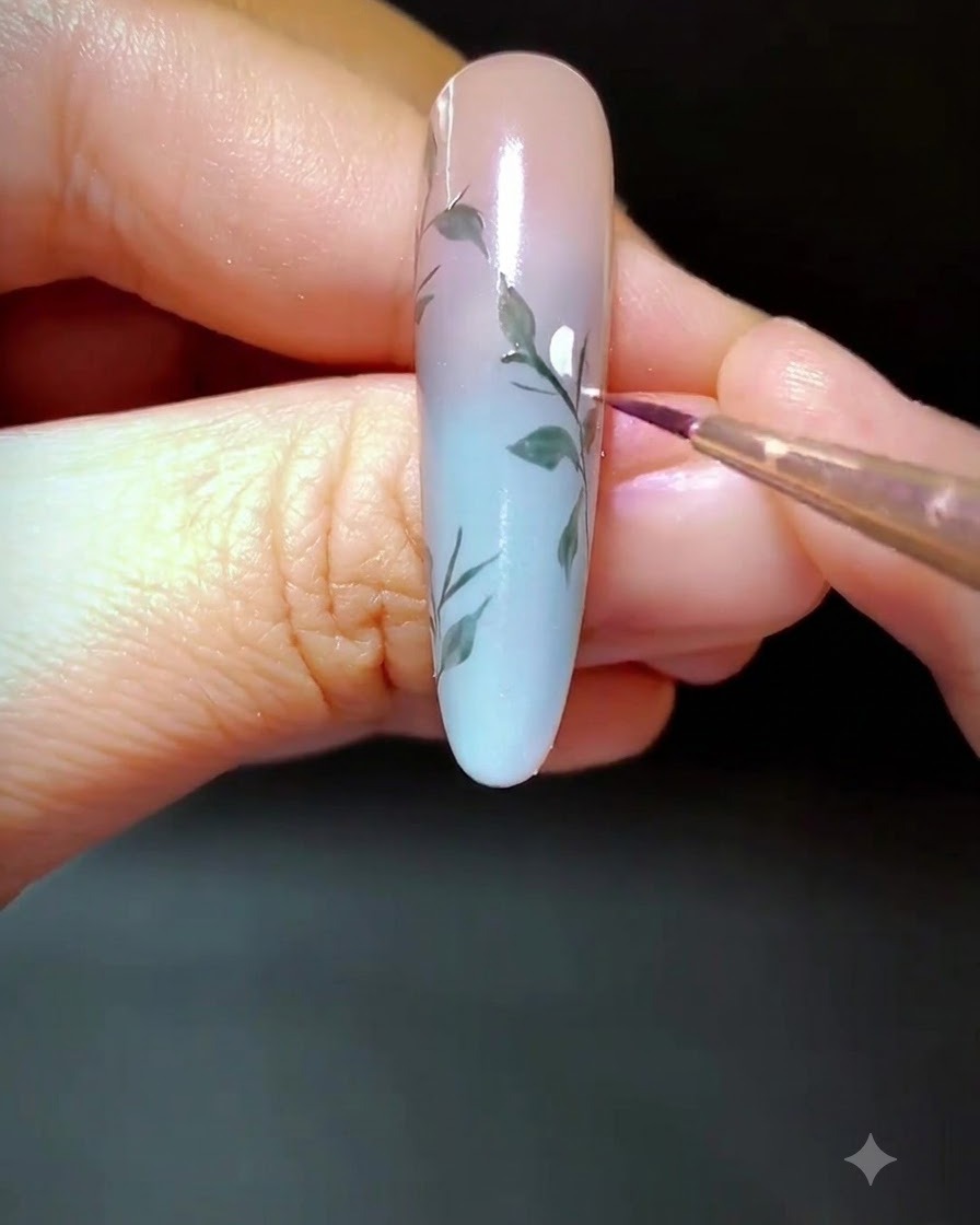 Gros plan sur un ongle décoré où de petits points de gel blanc sont appliqués le long de la branche peinte.