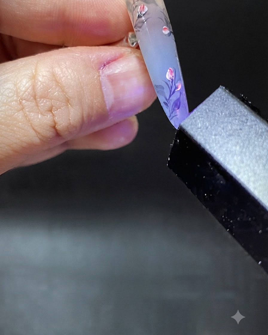 Un pinceau appliquant une goutte claire de gel de renforcement près des cuticules de longle décoré.