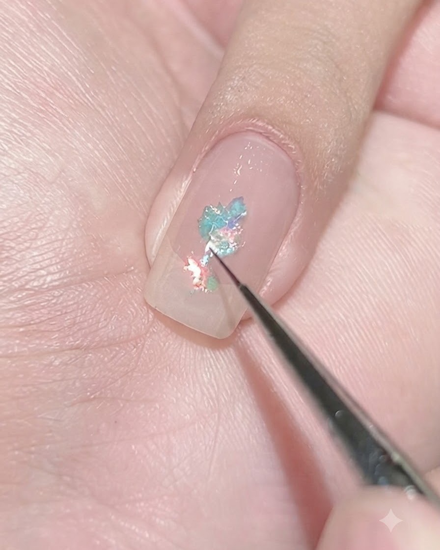 Un pinceau fin déposant de minuscules paillettes bleu clair sur un ongle recouvert de gel de base pour créer une grappe concentrée.