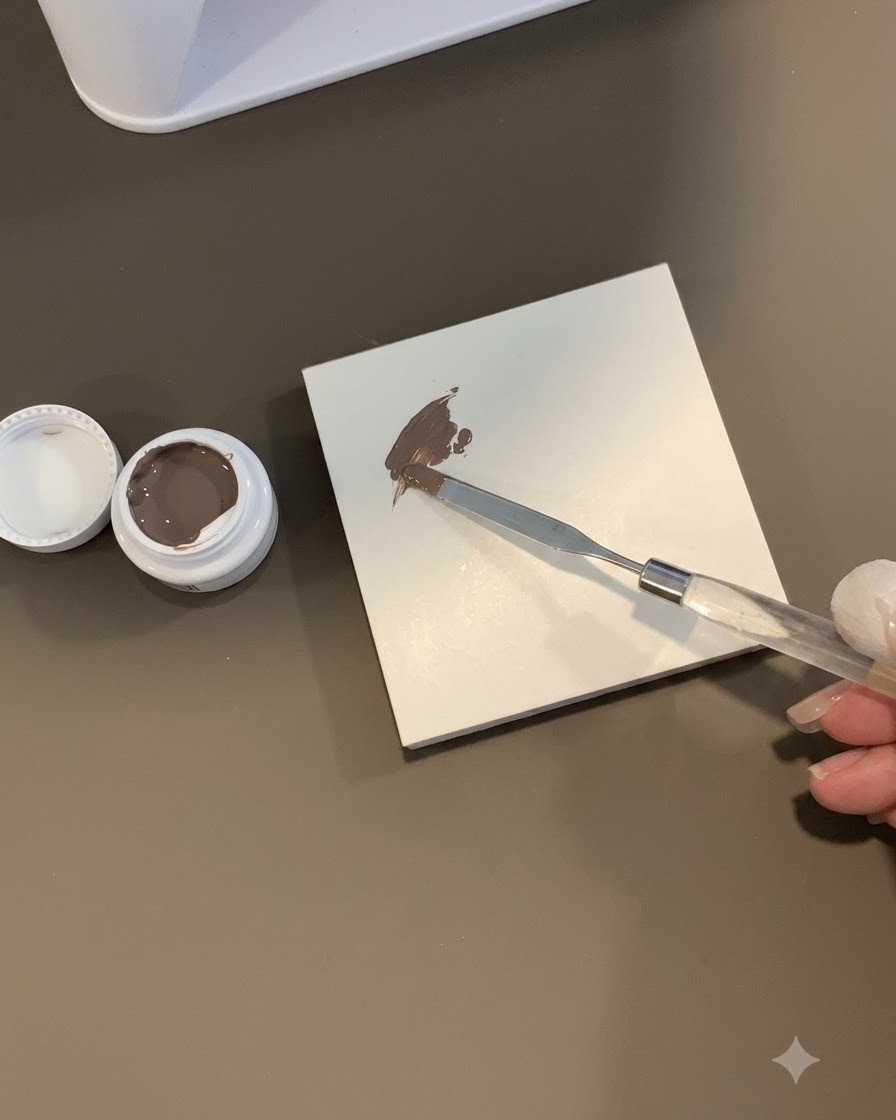 Un outil éponge tamponnant une tache de gel gris-marron sur une surface de carreau blanc.