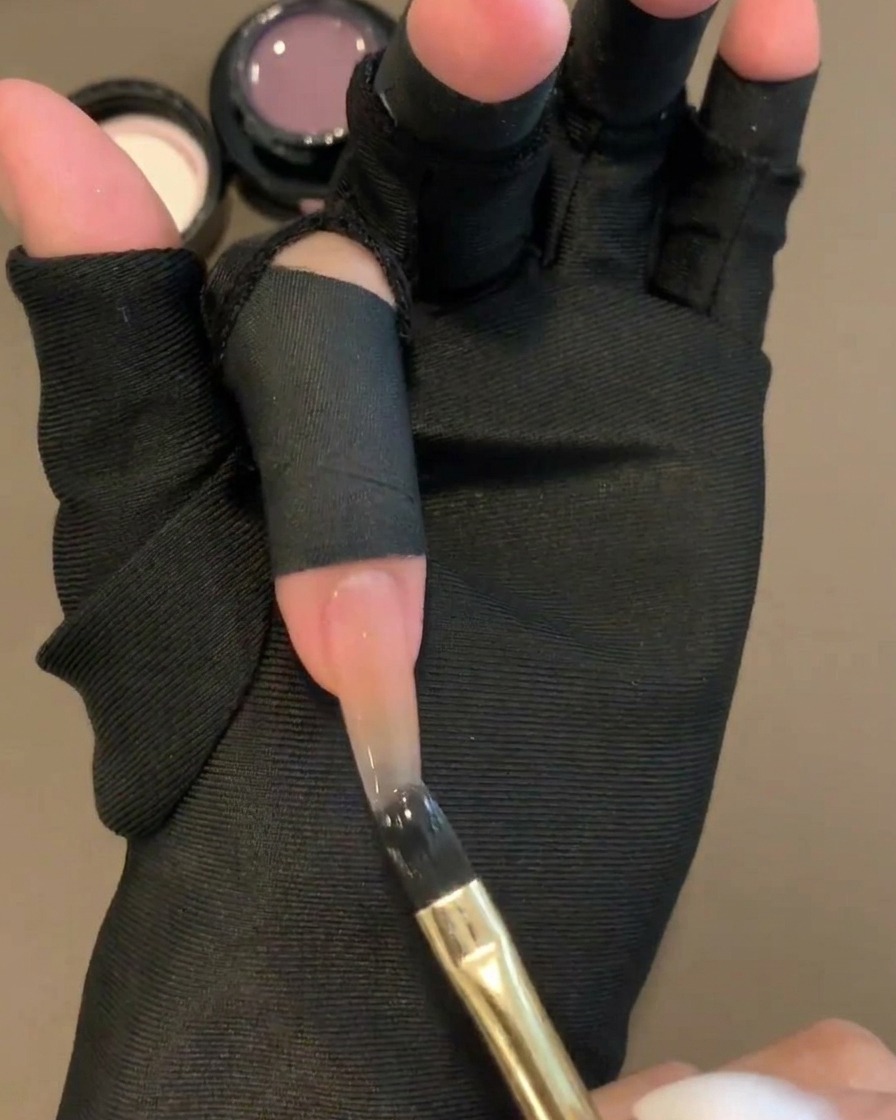 Un pinceau gel plat appliquant un gel de couleur violet diaphane sur la moitié supérieure dun ongle à base nude.