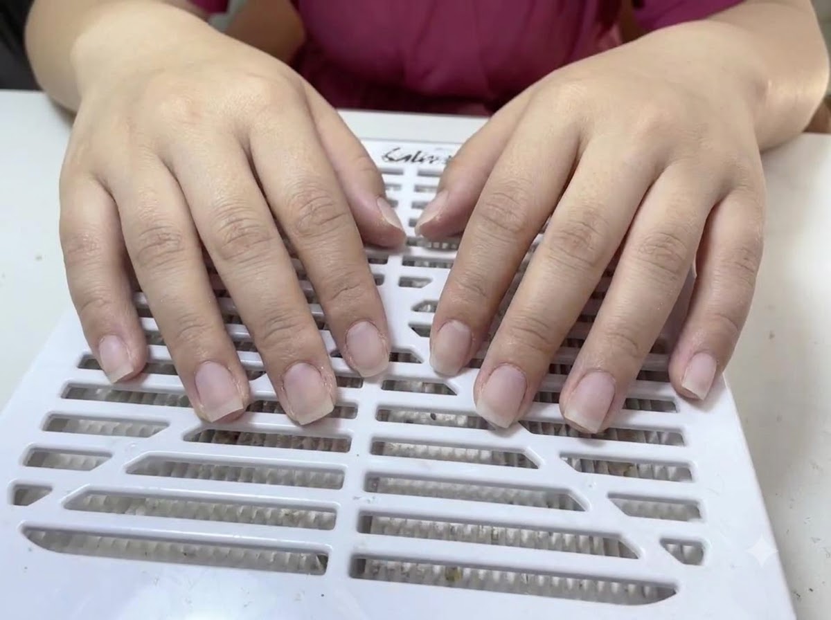 Deux mains aux ongles naturels nus et non vernis reposant sur une surface de dépoussiérage à fentes blanches.