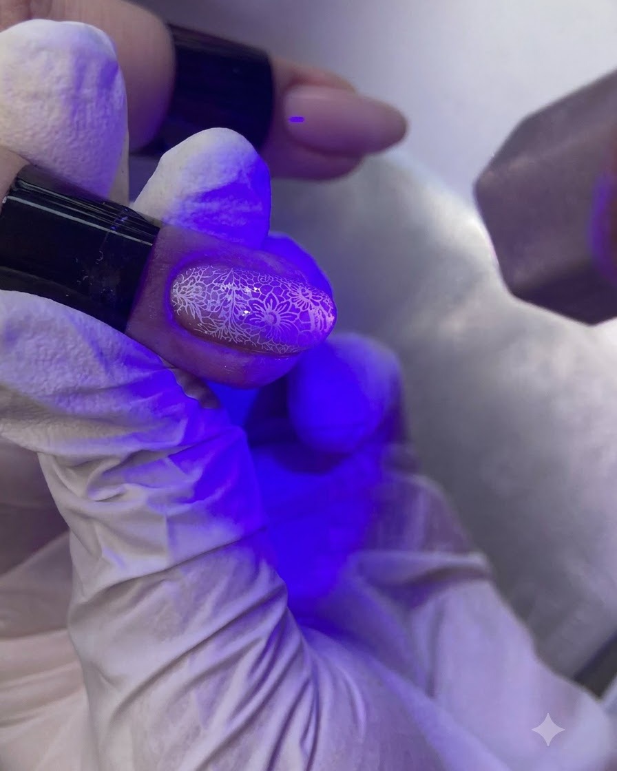 Une main sous une lampe à UV/LED pour ongles catalysant un ongle décoré.