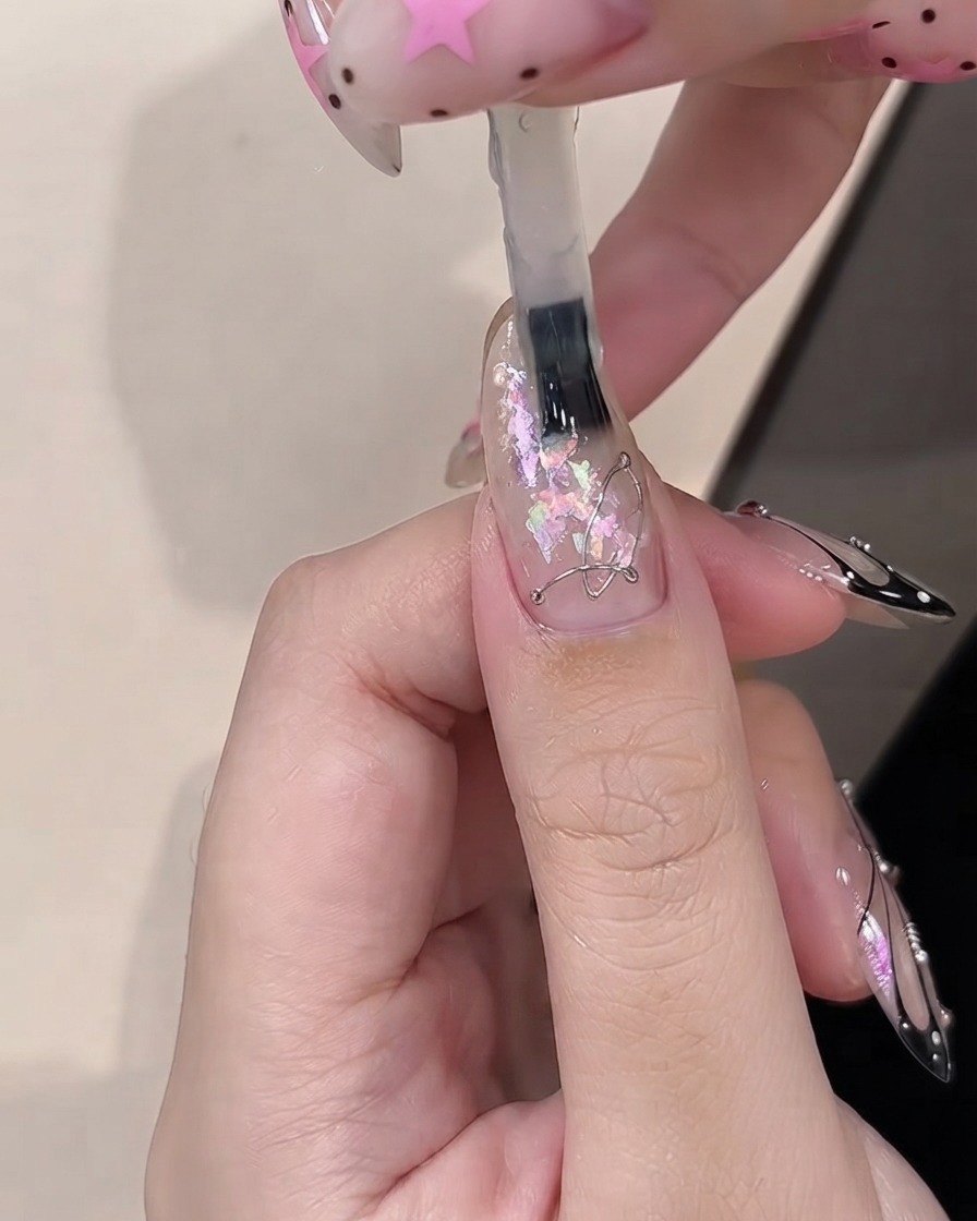 Un pinceau appliquant du gel de construction sur des morceaux dopale décoratifs intégrés sur un ongle enduit de clair.