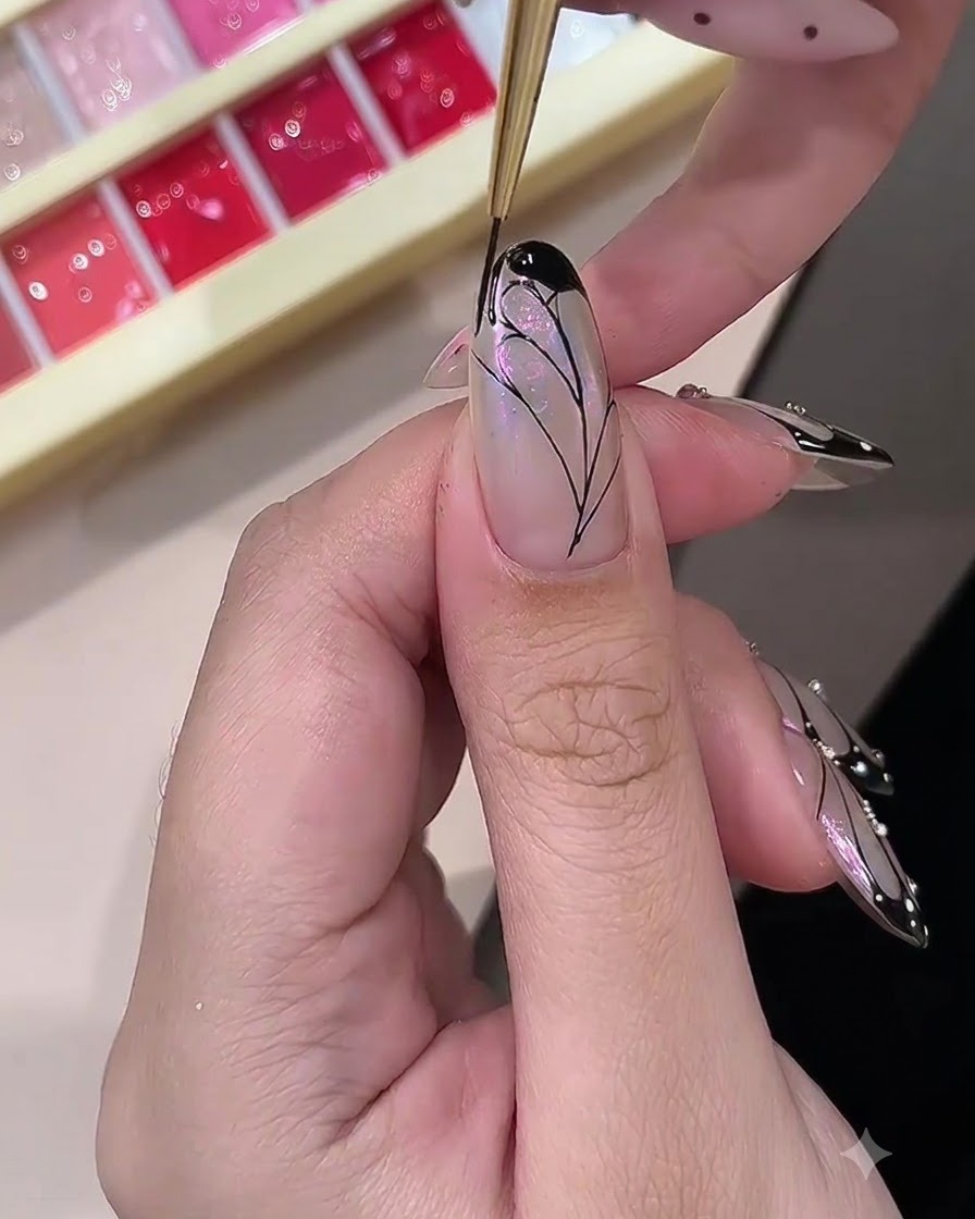 Une prothésiste ongulaire remplissant les bordures extérieures dun design daile de papillon peint avec du gel noir opaque.