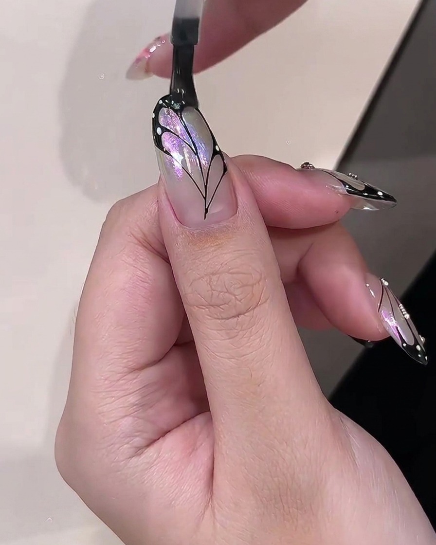 Un pinceau appliquant un top coat transparent brillant sur un design de nail art aile de papillon fini.