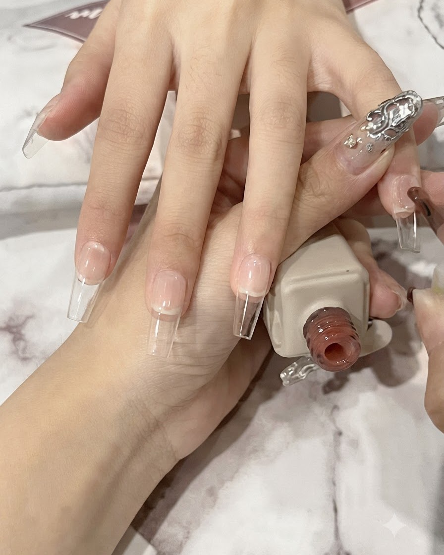 Un pinceau à ongles appliquant une fine couche de gel nude translucide sur une plaque dongle naturel long en forme de cercueil.