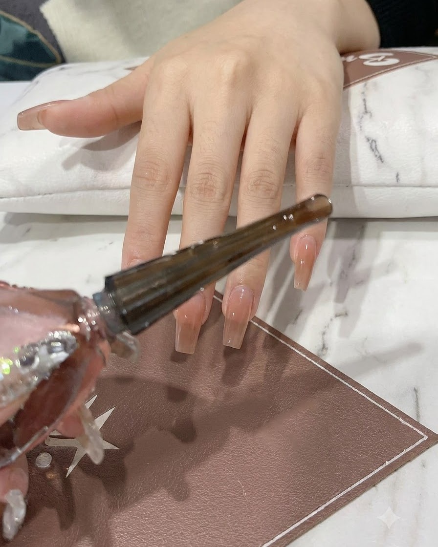 Une main tenant un flacon de gel rose et argent pailleté avec lembout pinceau étendu.