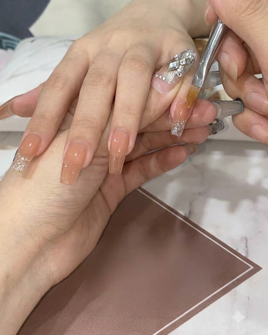 Un pinceau plat de détail plume et traîne des paillettes argentées vers le bas sur un ongle nude pour créer un dégradé lisse.