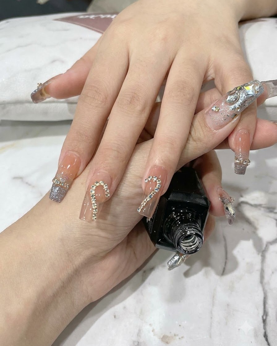Des pinces plaquant de petits strass scintillants à lintérieur dun contour de chaîne métallique sur un ongle.