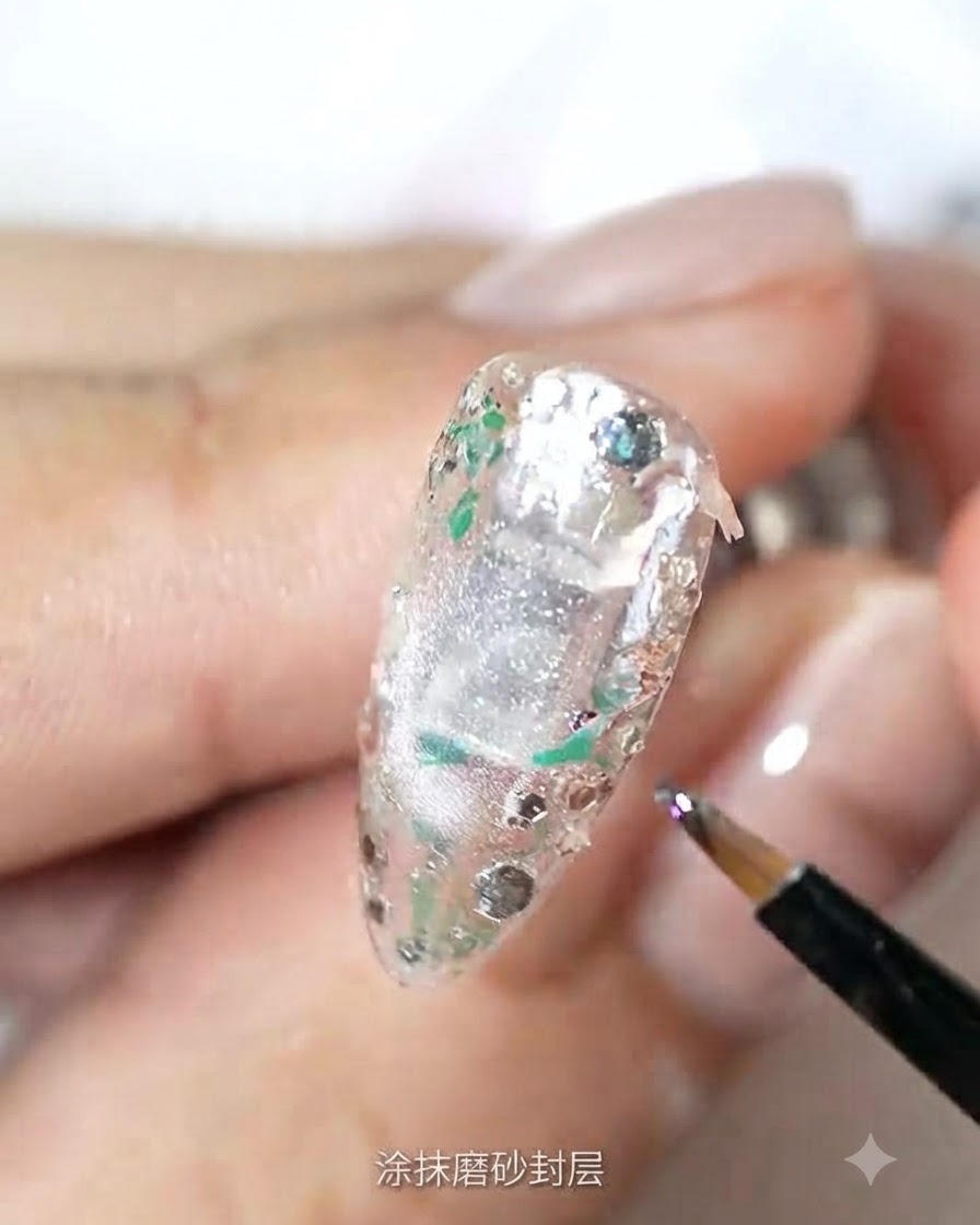 Un pinceau fin appliquant un top coat mat sur la surface dun ongle texturé et incrusté de paillettes.