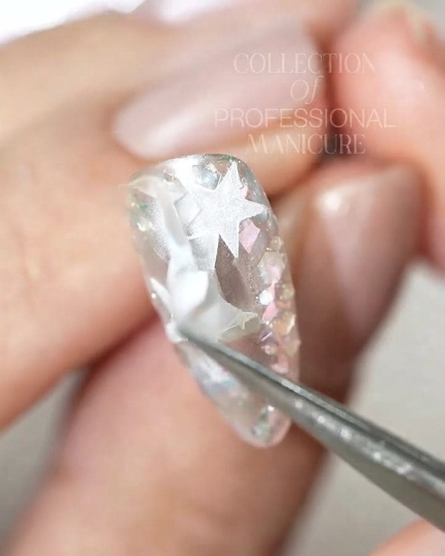 Une paire de brucelles retirant des morceaux complexes dautocollants détoiles blanches dun ongle brillant.