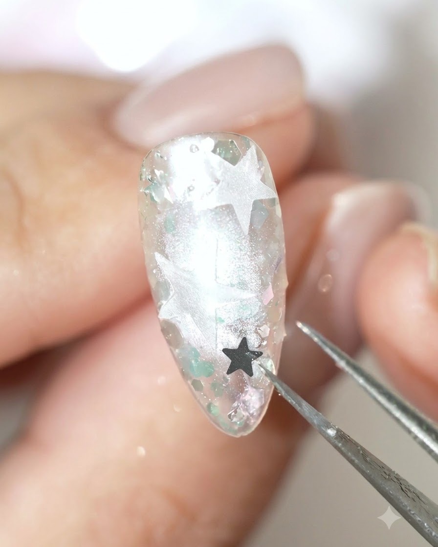Une paire de brucelles de précision plaçant un sequin détoile sombre sur la surface de longle décoré.