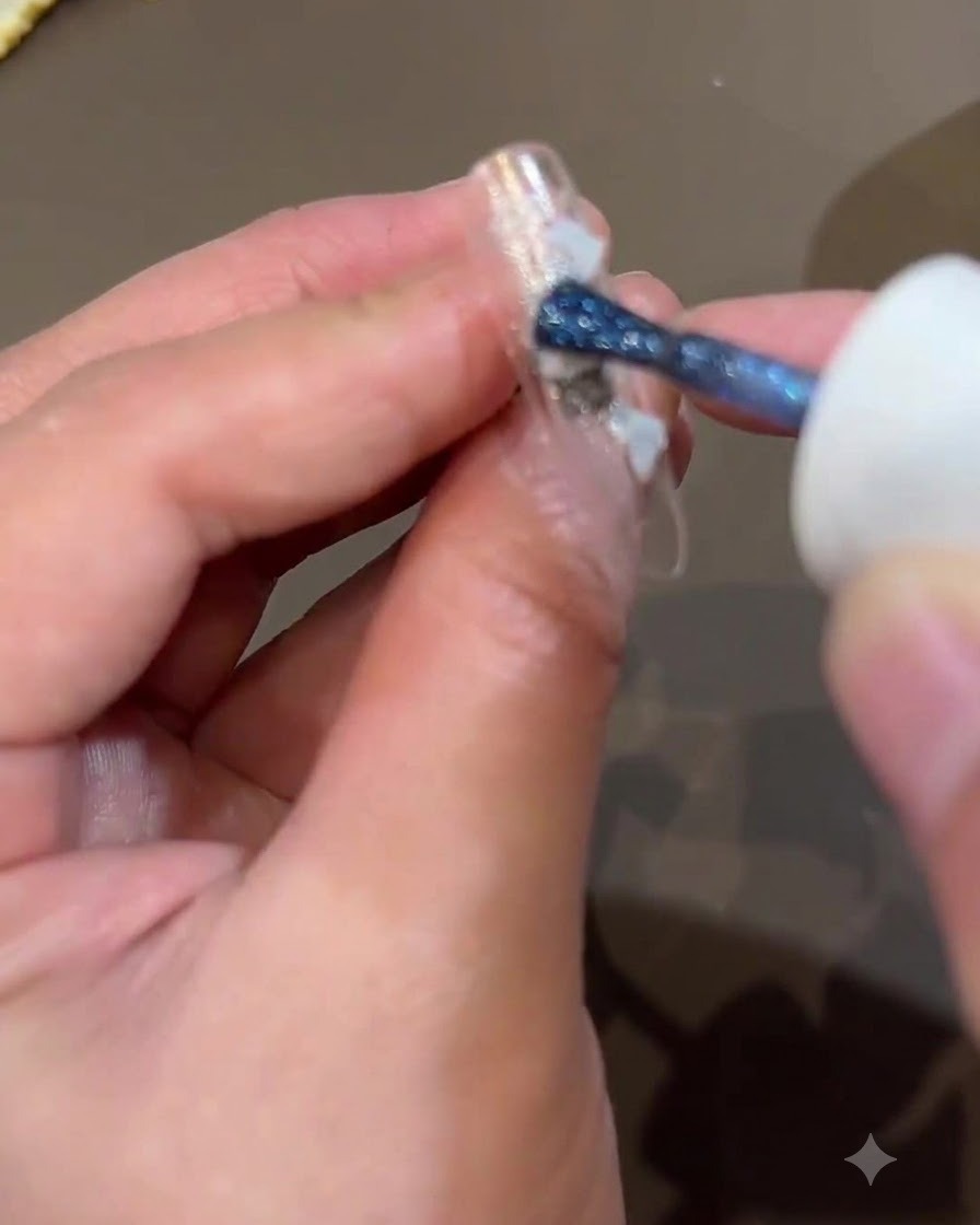 Un pinceau appliquant des paillettes bleu foncé sur la surface de longle pour ajouter de la profondeur au design.
