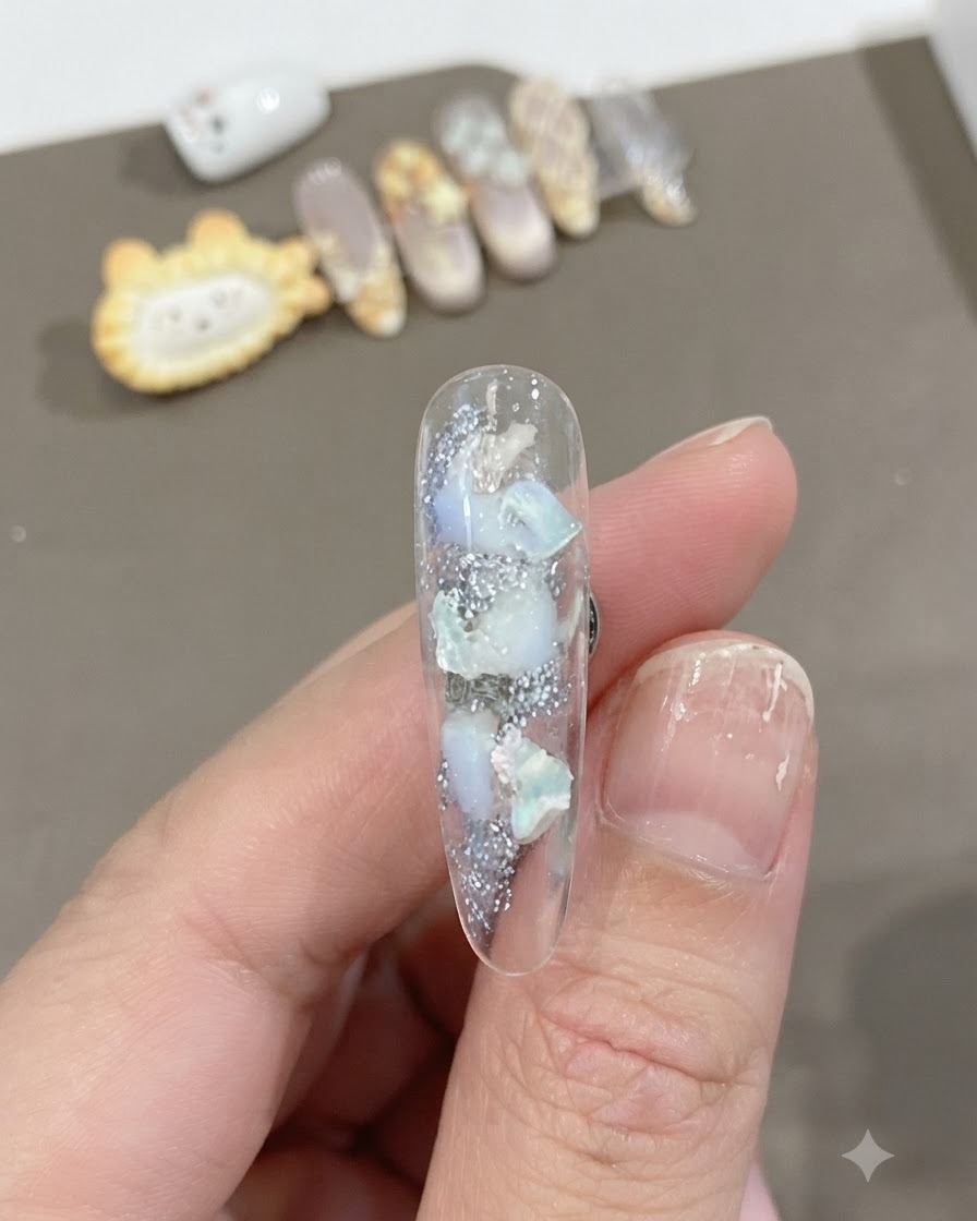 Gros plan dun ongle long transparent présentant des morceaux de coquillage incrustés et une texture chatoyante avec un fondu en dégradé blanc doux.