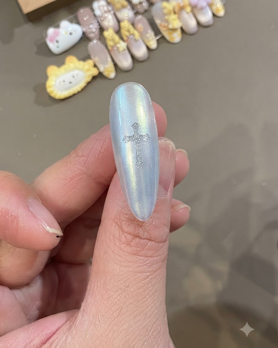 Gros plan dun ongle blanc nacré avec un autocollant de croix Chrome Heart argenté étincelant placé directement au centre.