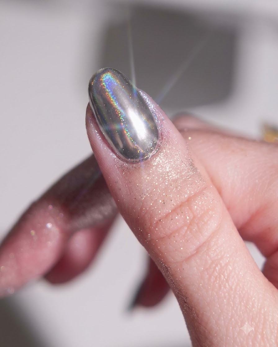 Un doigt avec une base gel noire catalysée frotté avec une poudre chrome argentée à laide dun applicateur éponge en silicone.