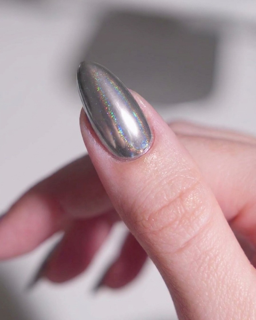 Un pinceau de maquillage doux balayant délicatement la poudre dargent métallique libre de la peau autour dun ongle chrome en amande.