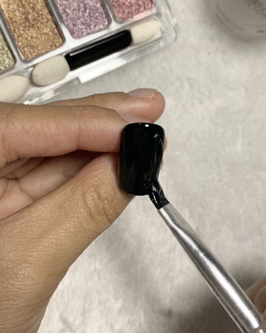 Un pinceau à tête fendue tirant des lignes verticales texturées en utilisant de la colle claire sur une surface dongle en gel noir.